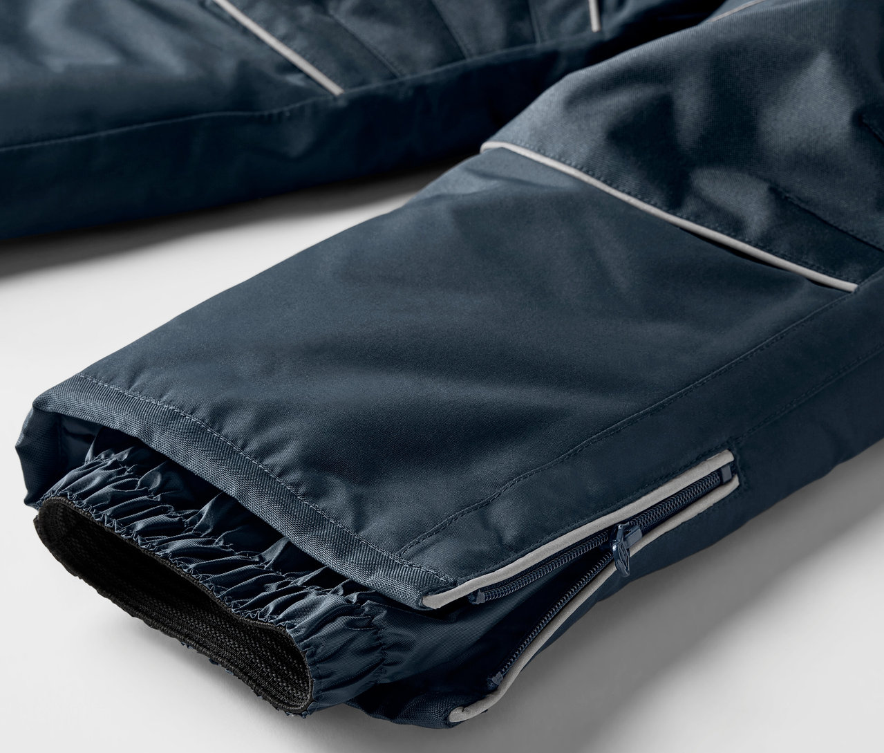 Gros plan sur le bas d'un pantalon de ski bleu marine avec des manchettes élastiques et une fermeture éclair.