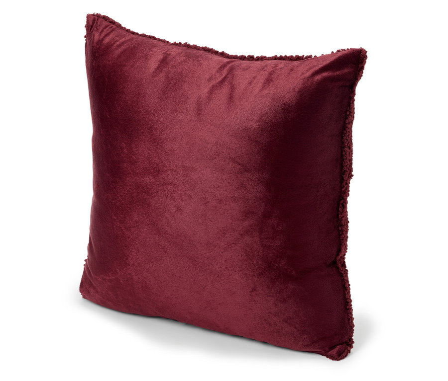 Un coussin en velours rouge avec une bordure décorative repose sur une surface blanche.