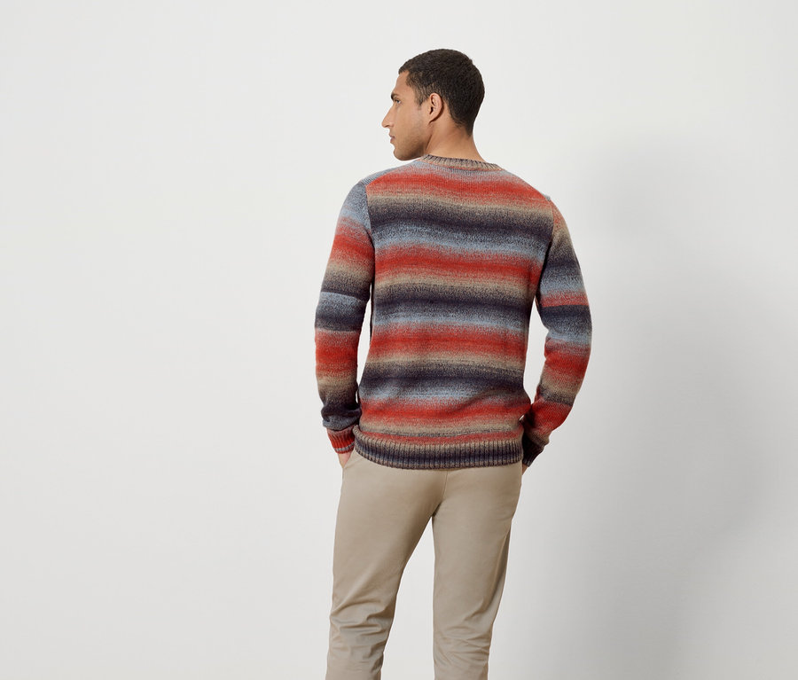 Un homme, dos à la caméra, porte un pull rayé et un pantalon.