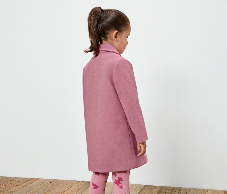 Fillette portant un manteau rose et un legging à motif étoile, debout dos à la caméra.