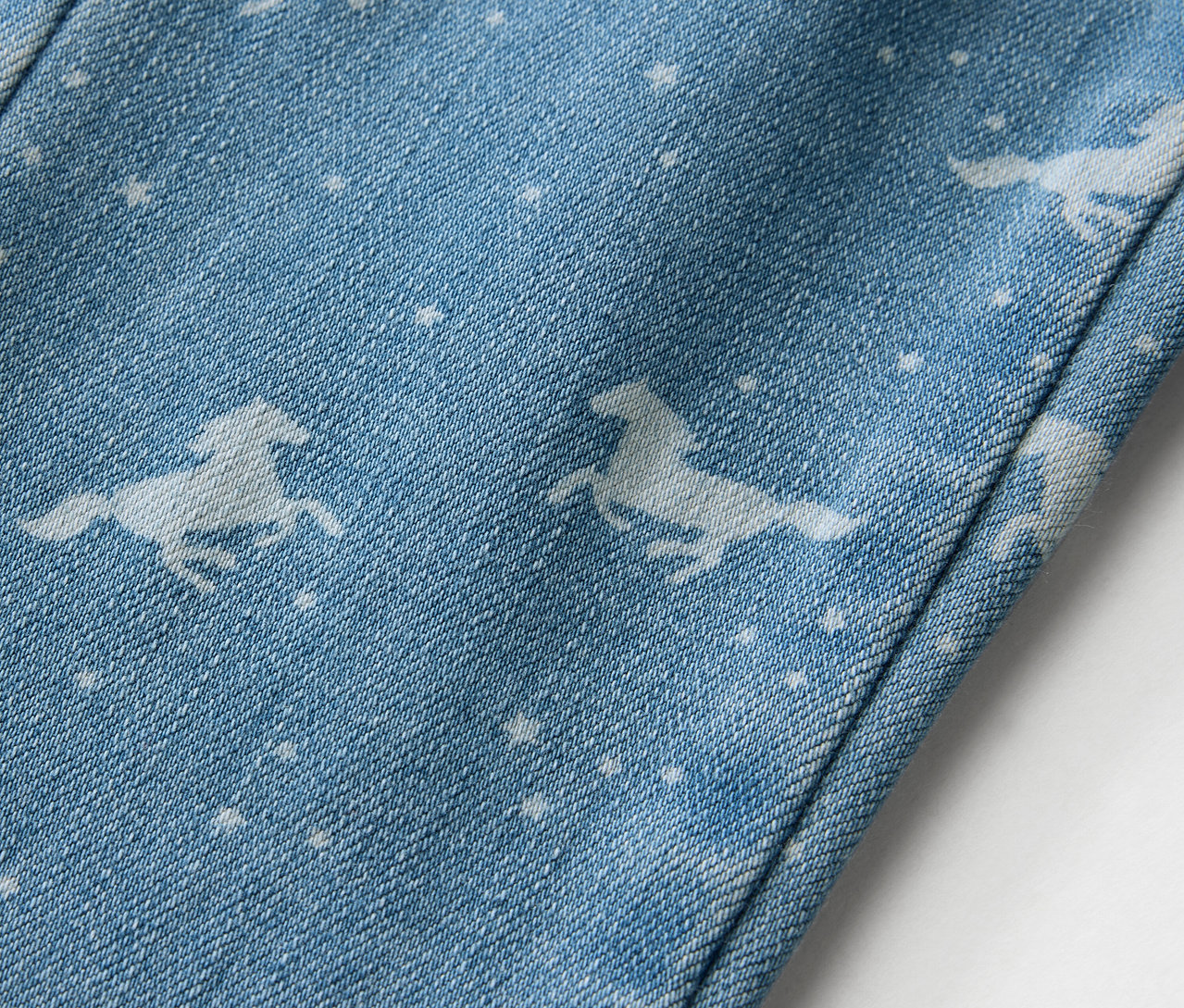 Détail d'un tregging pour enfant avec des motifs de chevaux et d'étoiles sur un fond bleu clair.