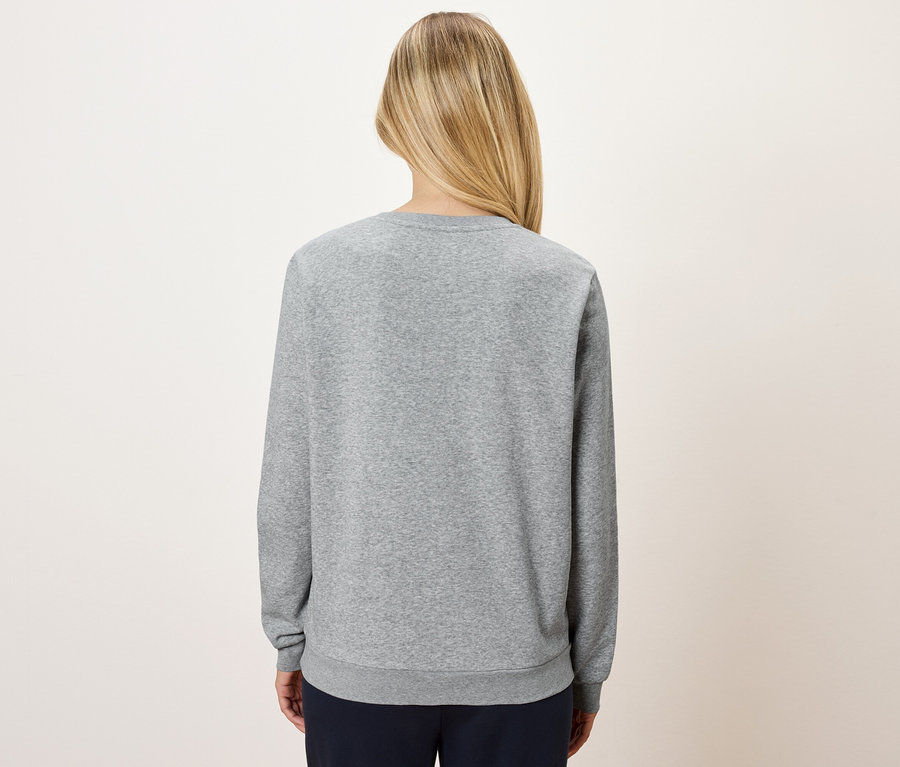 Vue arrière d'une femme blonde portant un pull gris et un pantalon bleu marine.