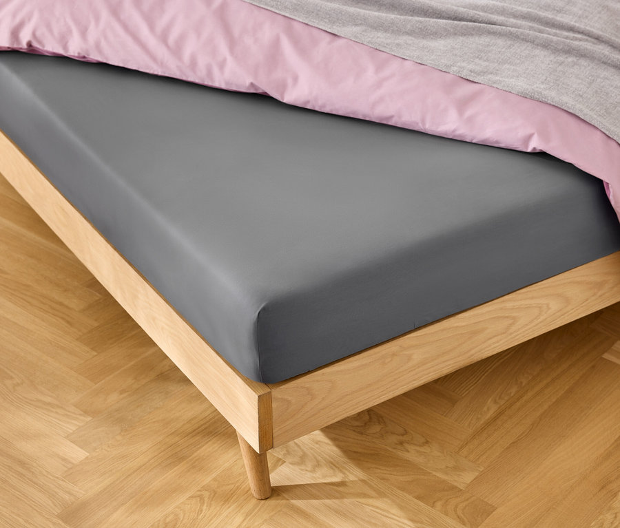 Lit avec drap-housse gris, linge de lit rose et couverture grise.