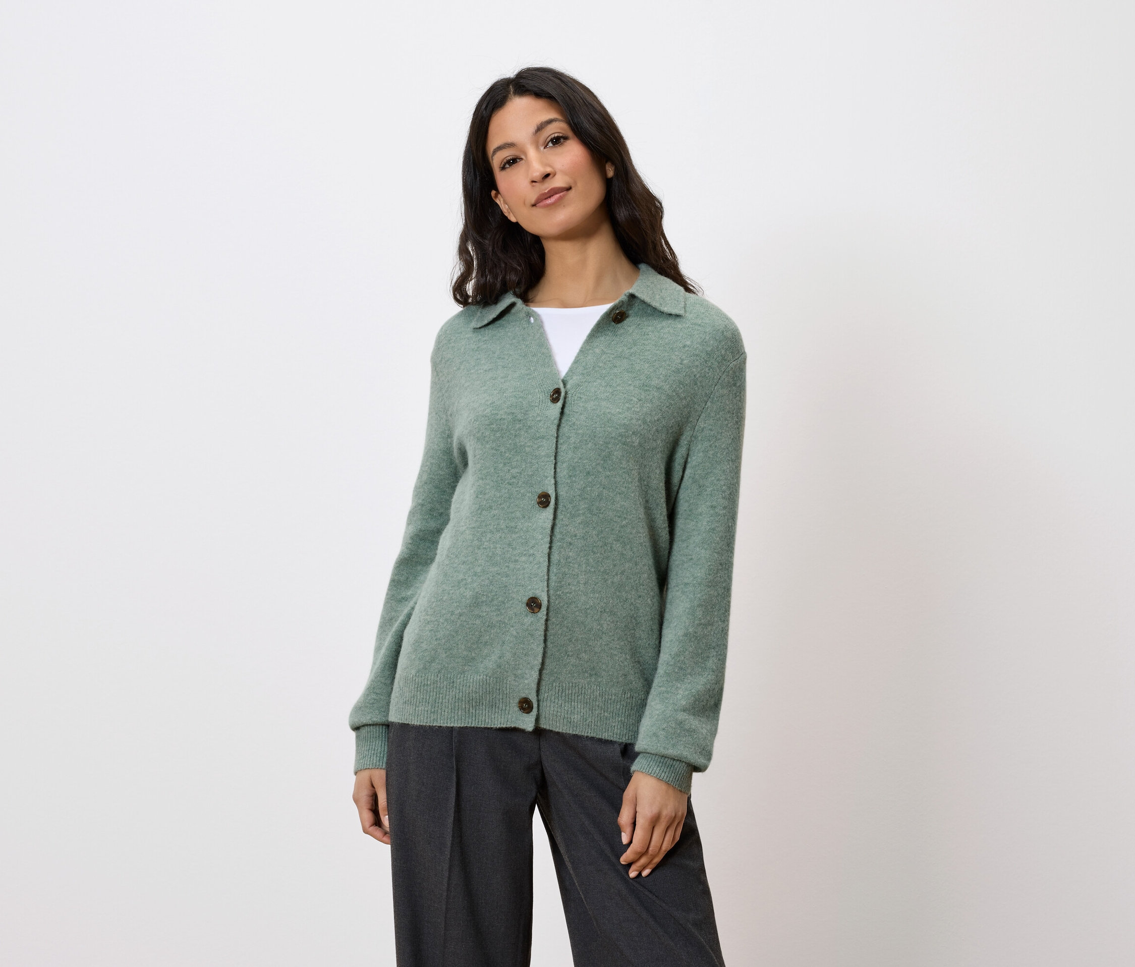 Une femme porte un cardigan vert boutonné et un pantalon gris.