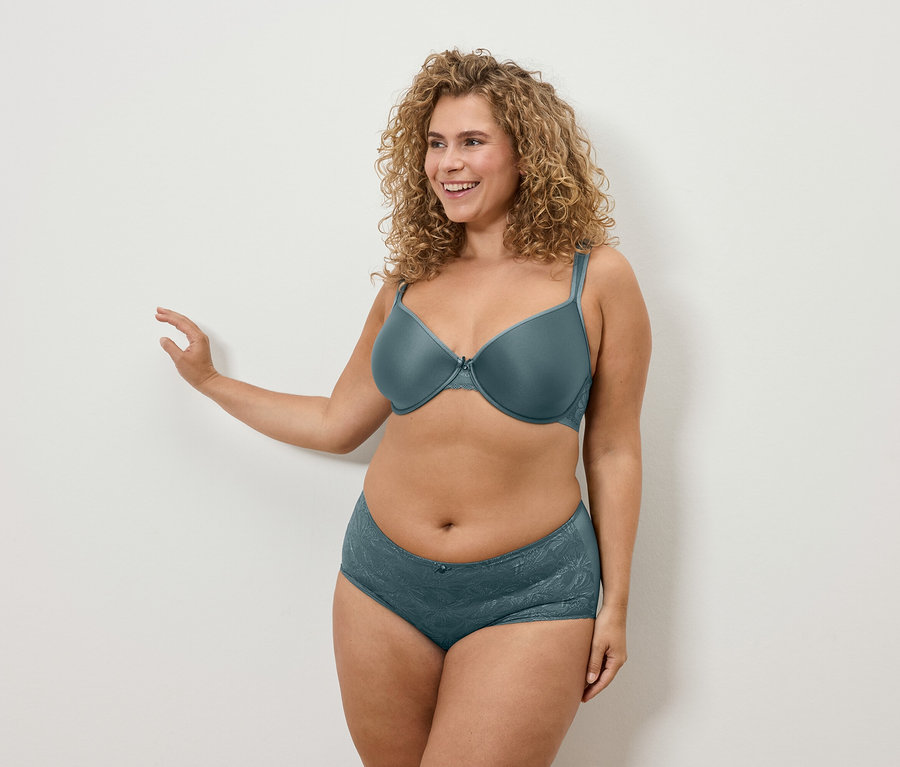 Une femme aux cheveux bouclés pose en soutien-gorge et culotte bleu-vert.
