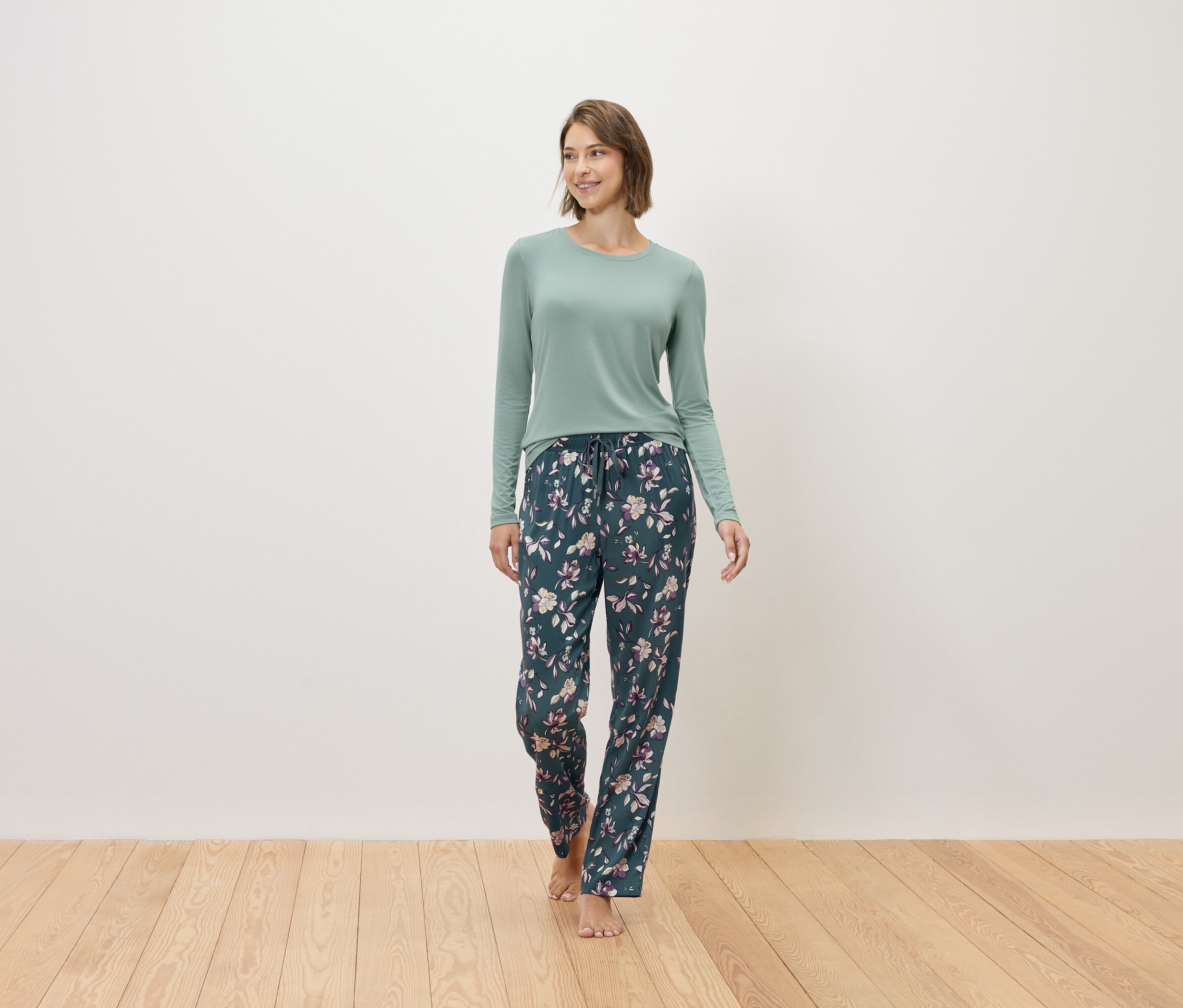 Une femme marche pieds nus, vêtue d'un pull menthe et d'un pantalon de pyjama bleu marine à motifs floraux.