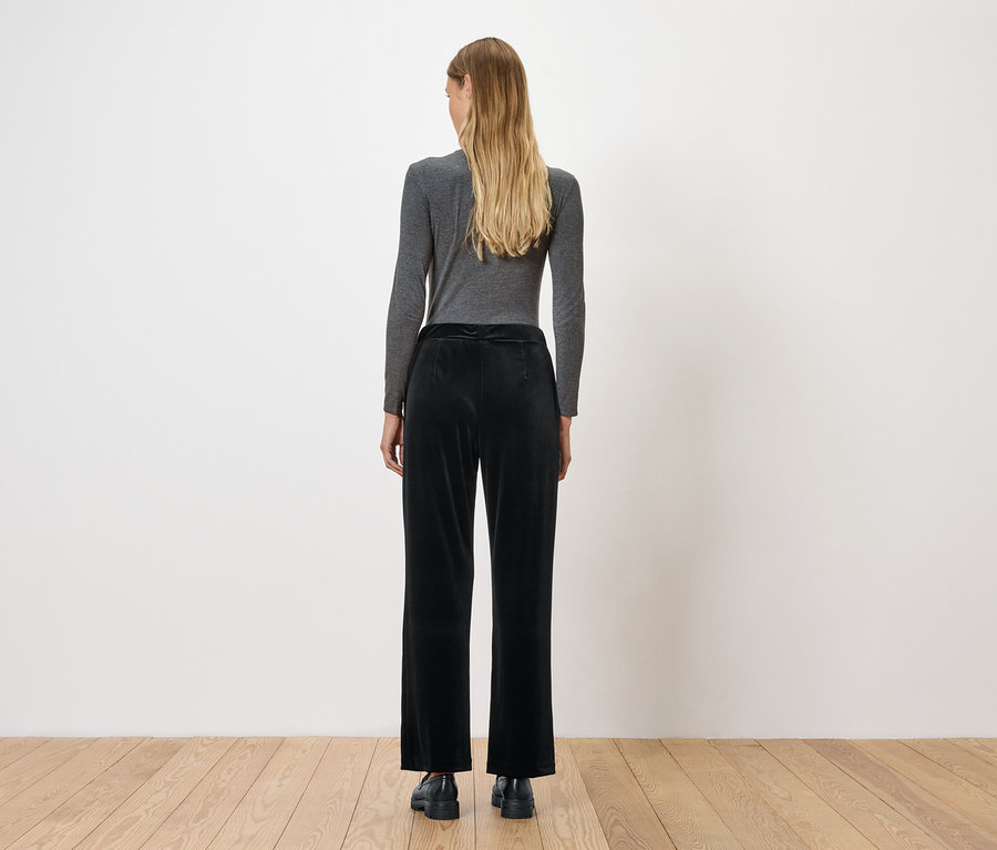 Une femme, vue de dos, porte un t-shirt gris à manches longues et un pantalon de velours noir.