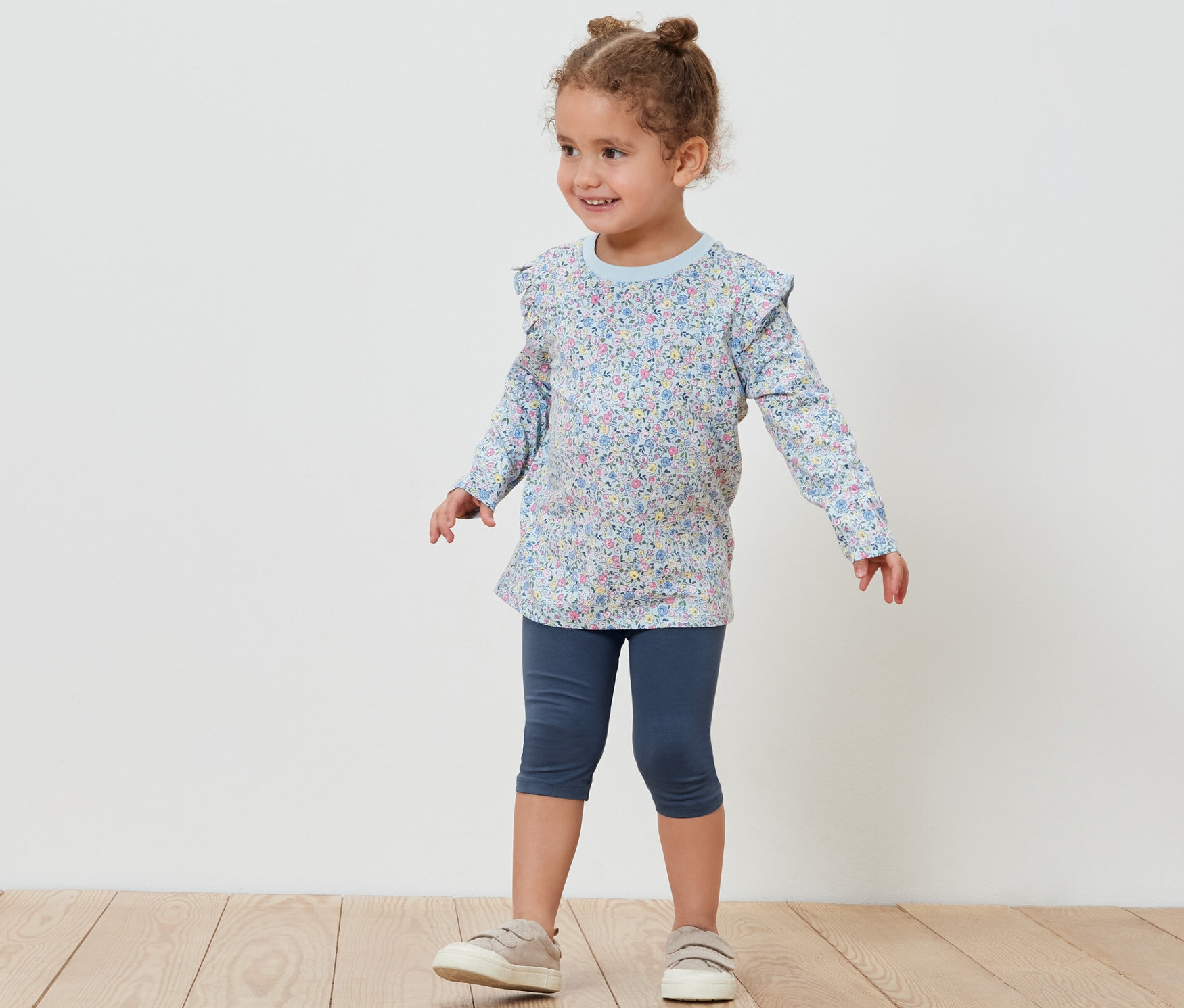 Une petite fille pose en leggings 3/4 et un chemisier à fleurs. Un des 5 leggings 3/4 pour enfant est visible.