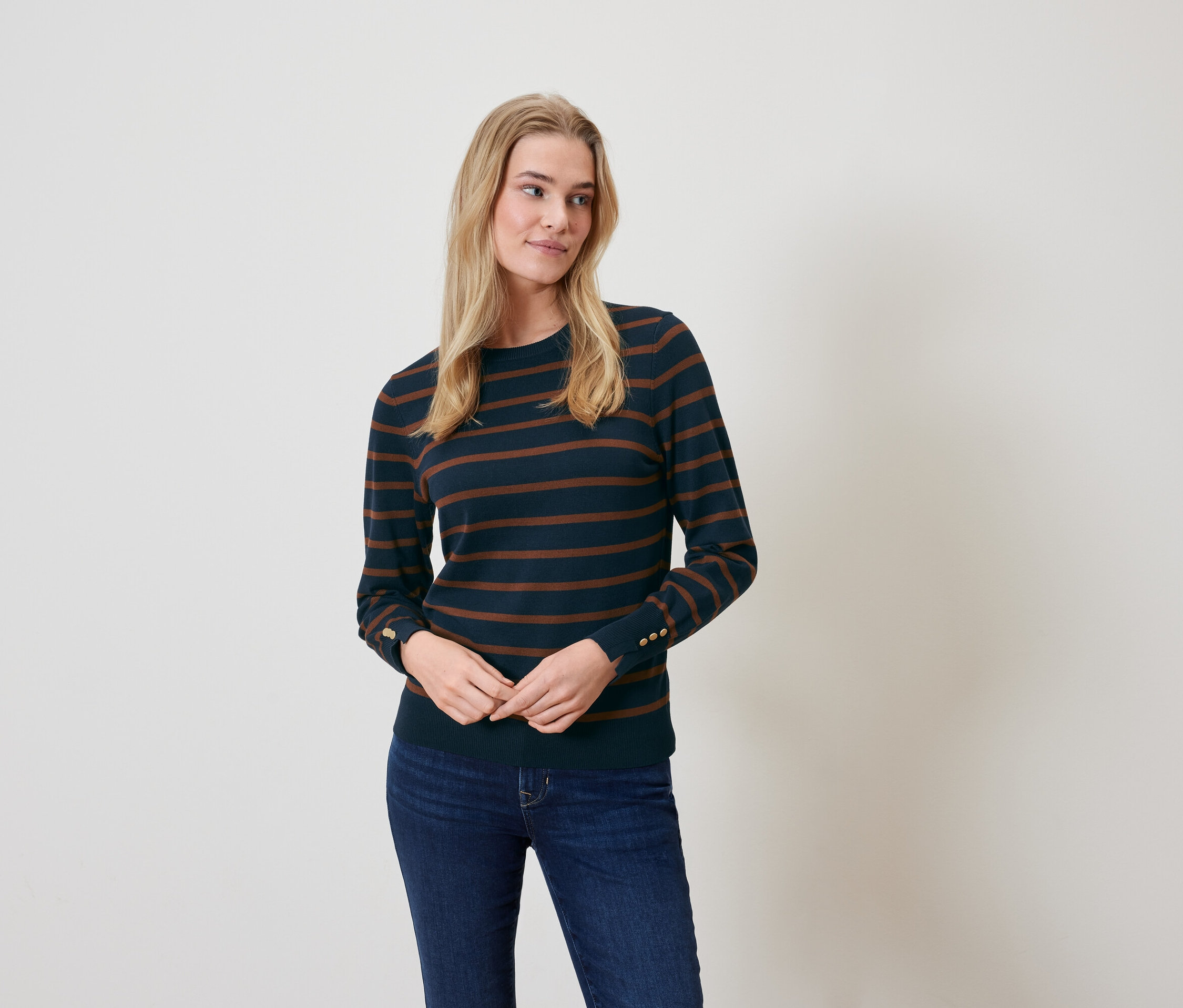 Une femme blonde pose en pull rayé et jean.