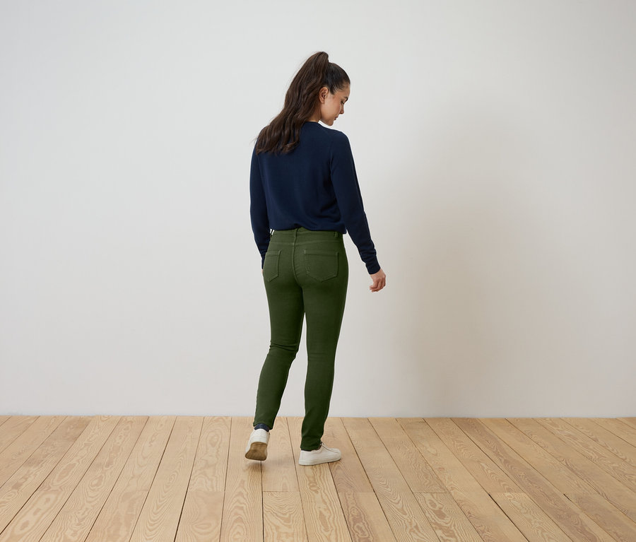Une femme, vue de dos, porte un pull bleu marine et un jean vert.