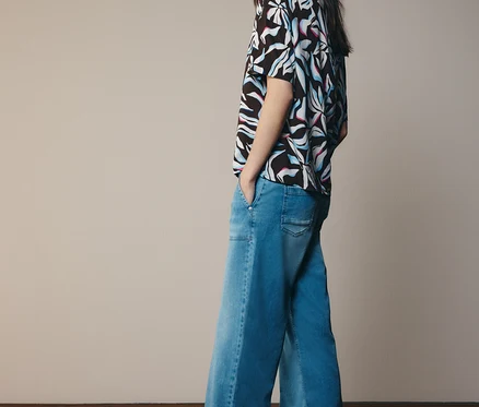 Femme portant un haut à motifs et un jean évasé, regardant sur le côté.
