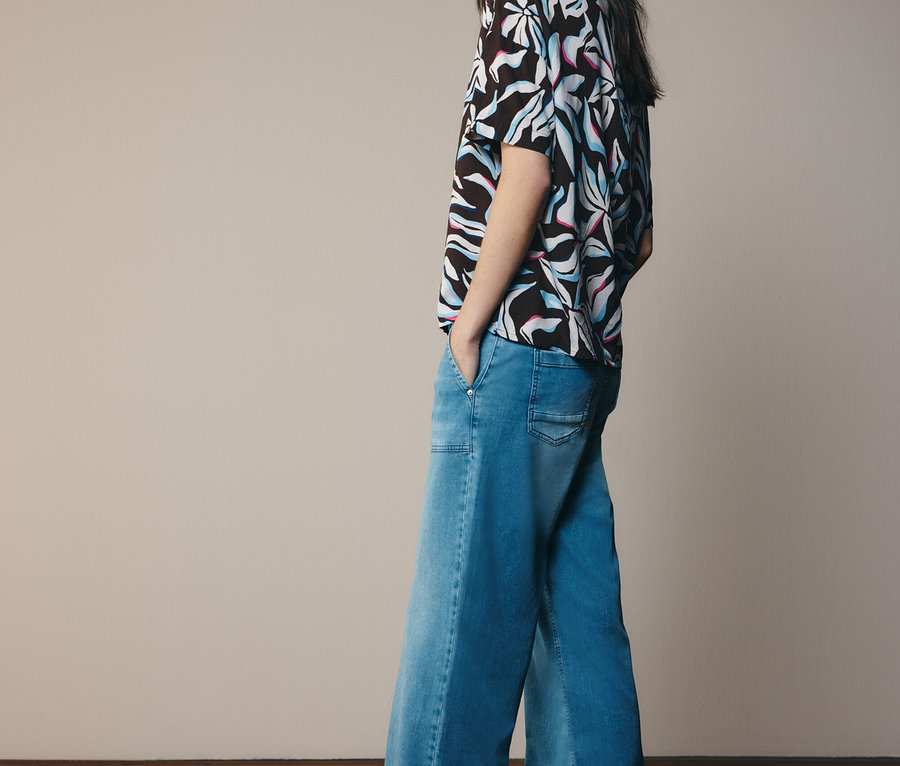 Femme portant un haut à motifs et un jean évasé, regardant sur le côté.