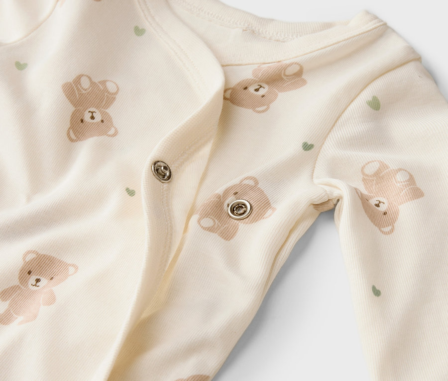 Gros plan d'une grenouillère claire pour bébé avec des motifs d'ours et de cœurs et des boutons-pression.