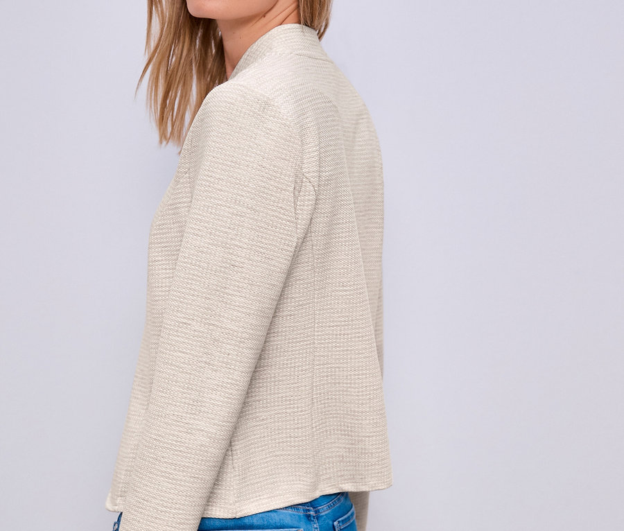 Femme blonde portant un blazer en jersey Street One clair et un jean bleu, regardant par-dessus son épaule.