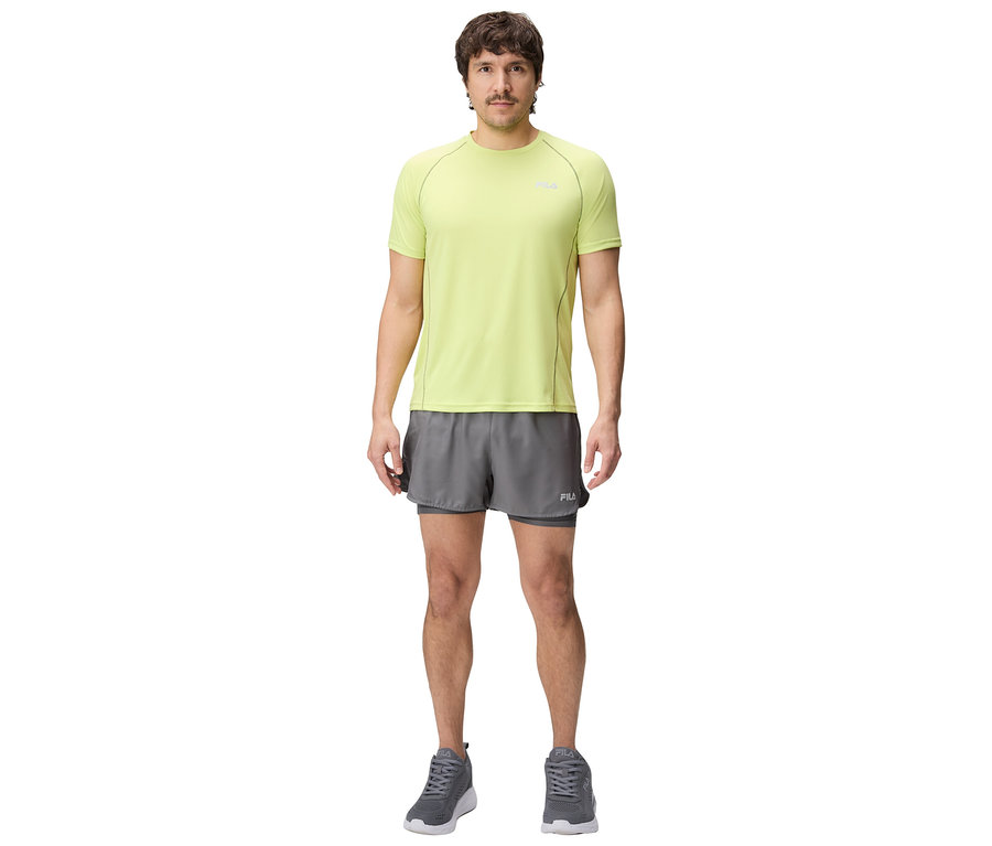 Homme debout portant un t-shirt vert clair, un short gris et des baskets grises.