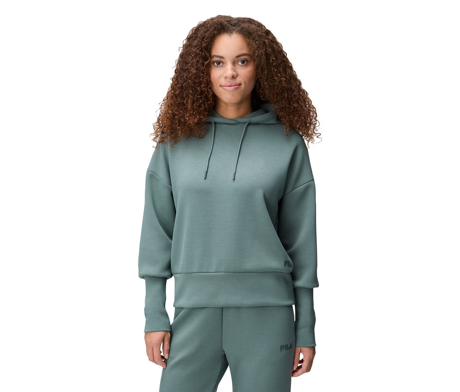 Une femme aux cheveux bouclés porte un sweat à capuche vert et un pantalon de jogging assorti.