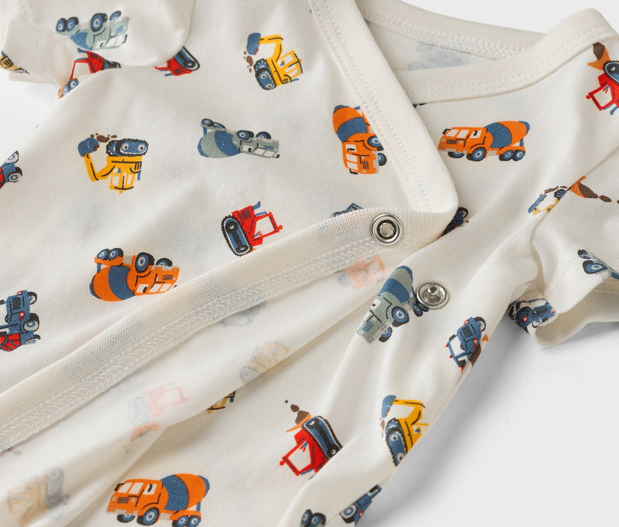 Gros plan sur un body blanc pour bébé avec un motif de camions de construction.
