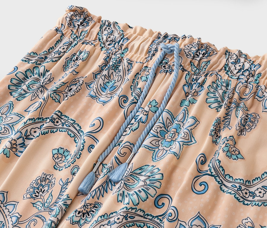 Gros plan d'un pantalon pêche avec un motif floral bleu et un cordon de serrage.