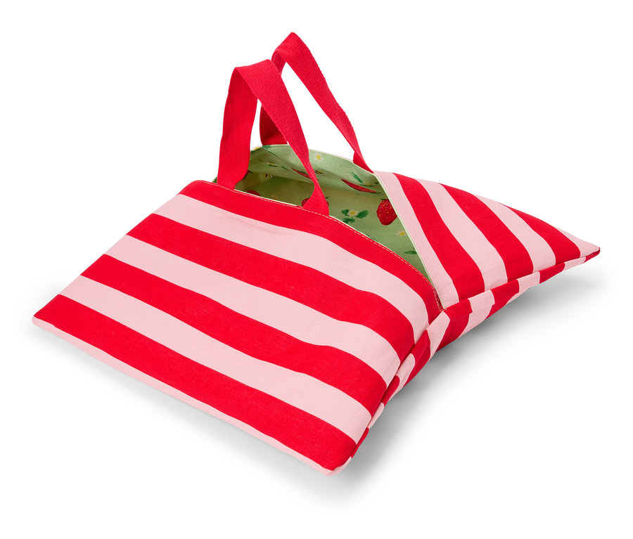 Un sac rayé rouge et blanc avec des poignées rouges et une doublure intérieure verte avec un motif de fraises est posé sur une surface blanche.