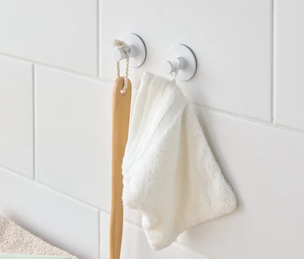 Une brosse de bain et une serviette blanche sont suspendues à des crochets blancs sur un mur carrelé blanc.
