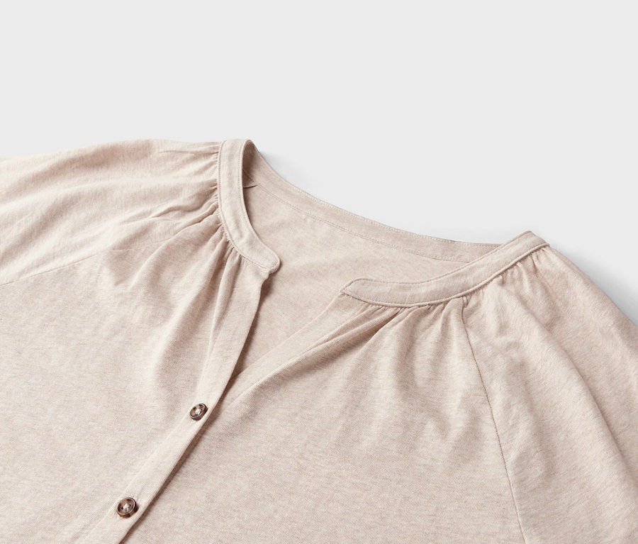 Gros plan d'une chemise beige à manches longues, boutonnée, avec des manches froncées sur fond blanc.