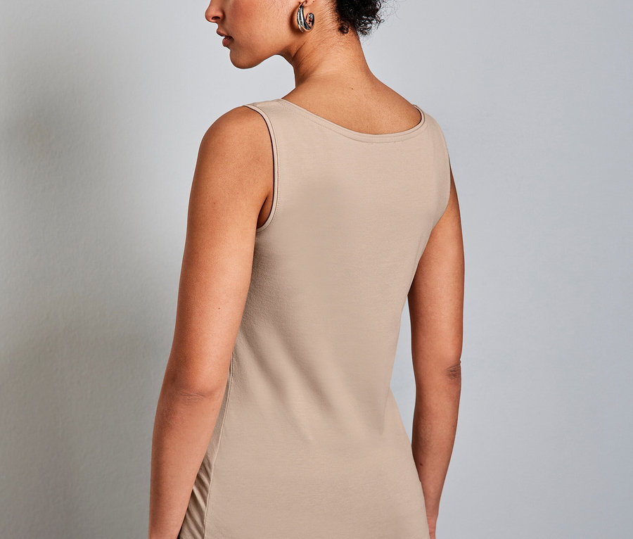 Femme aux cheveux courts et bouclés, vue de dos, portant un haut classique Street One beige et un jean bleu.