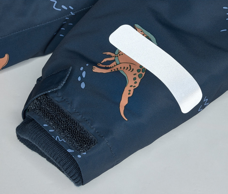 Gros plan sur une manche bleu marine avec motif de dinosaures, fermeture velcro et bande réfléchissante.