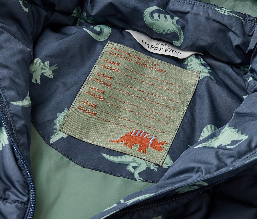 Vue intérieure d'une veste bleu-vert avec un motif de dinosaures et une étiquette avec de l'espace pour le nom et le numéro de téléphone.