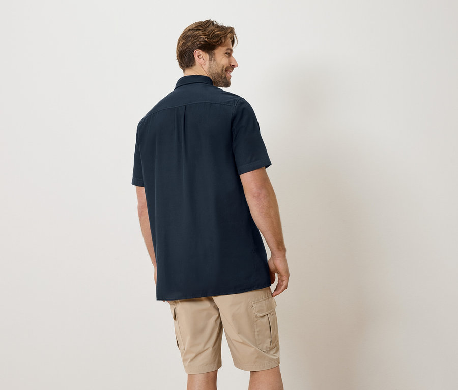 Homme de dos en chemise bleu marine et short beige.