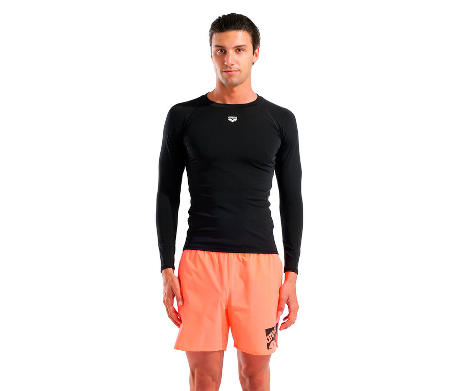 Un homme debout, portant un T-shirt noir à manches longues et un short orange.