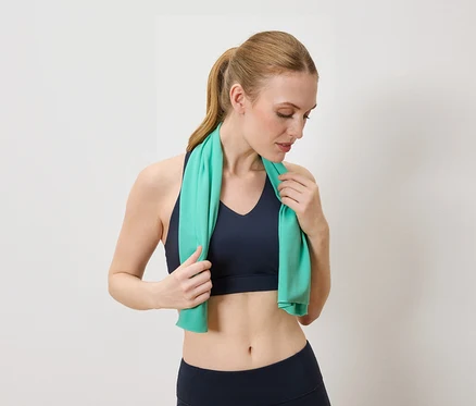 Femme portant un soutien-gorge de sport bleu et un legging tenant une serviette turquoise autour du cou.