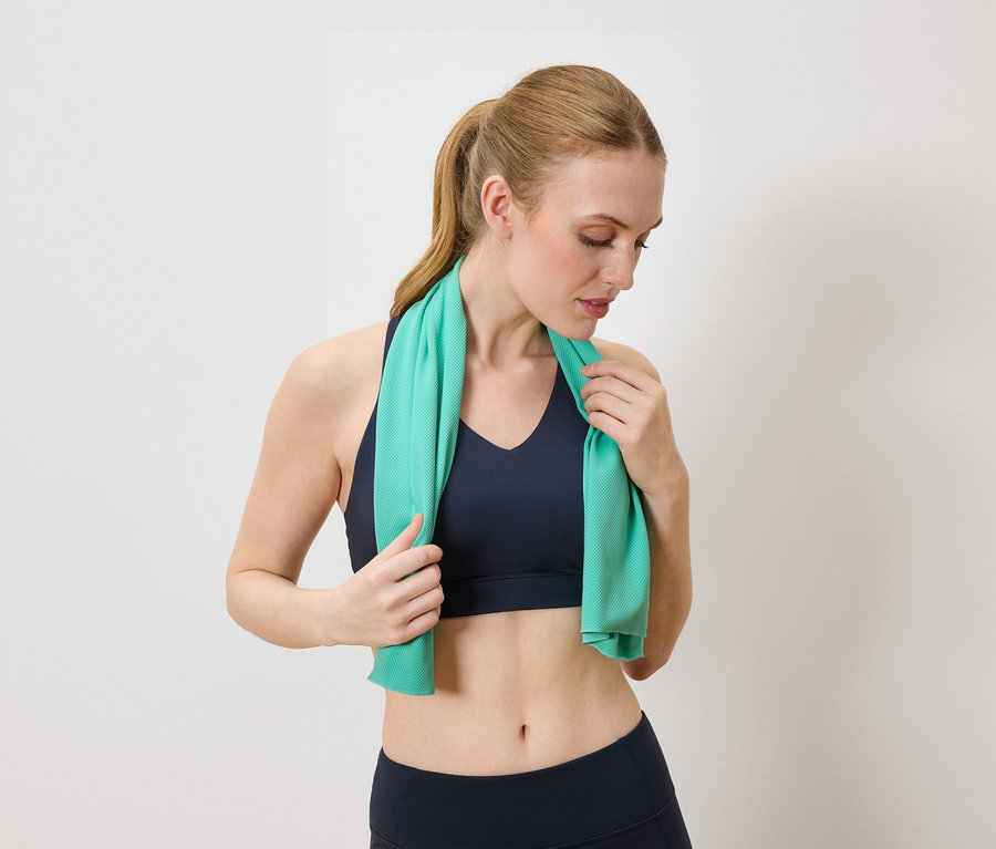 Femme portant un soutien-gorge de sport bleu et un legging tenant une serviette turquoise autour du cou.
