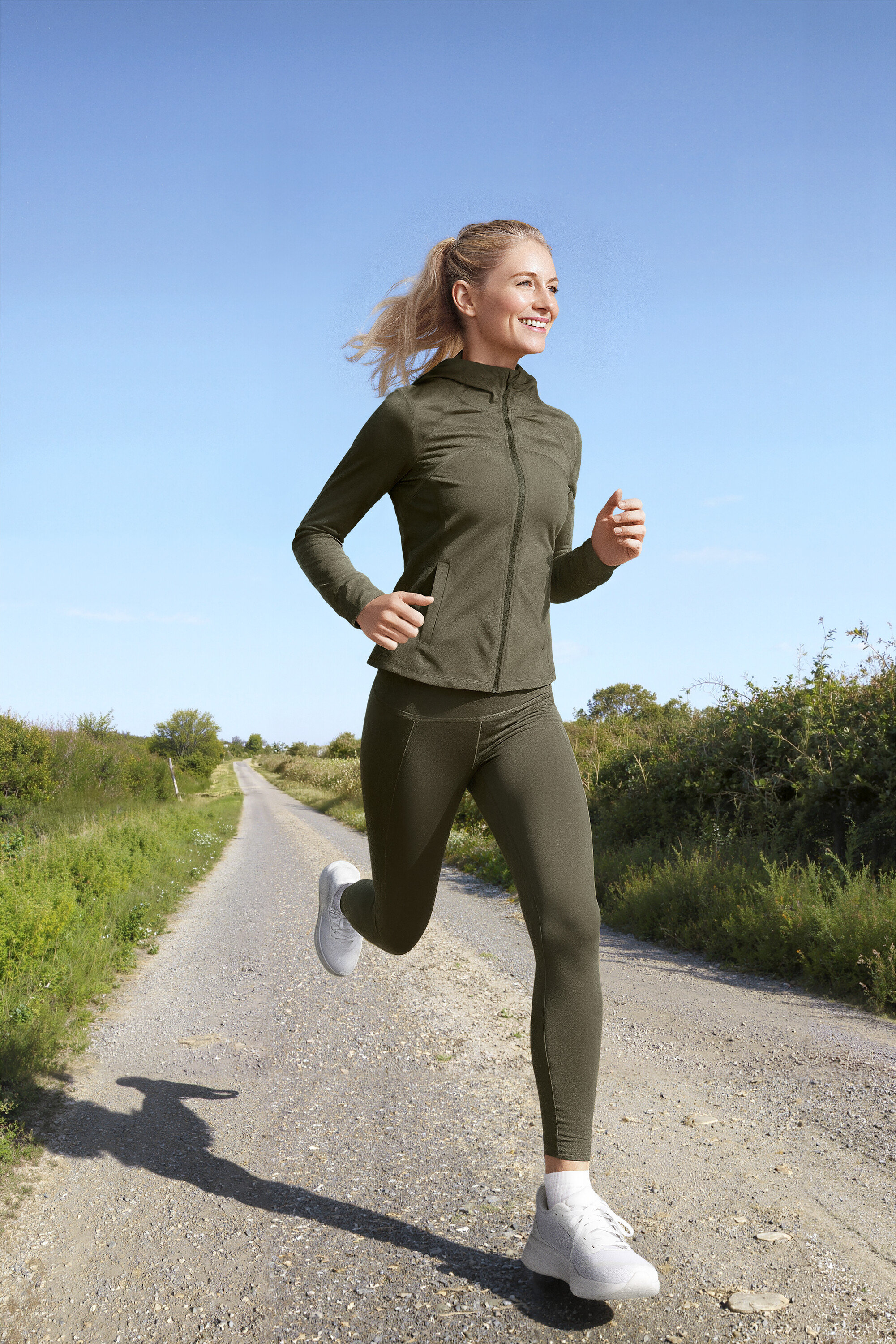 Femme courant sur un chemin de terre, elle porte une veste de sport, un legging de sport »ActivePower« et un t-shirt de sport lime.