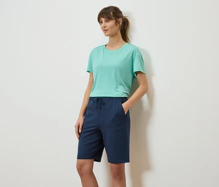Femme avec queue de cheval, porte un t-shirt turquoise et un short bleu marine.