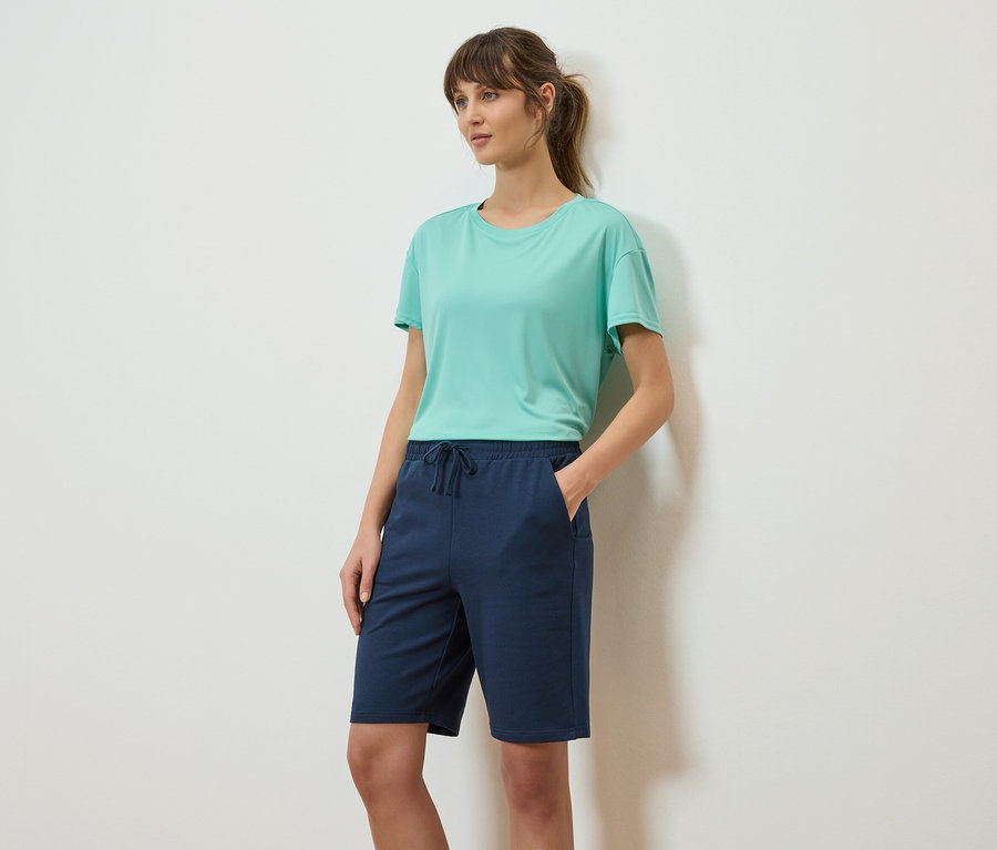 Femme avec queue de cheval, porte un t-shirt turquoise et un short bleu marine.