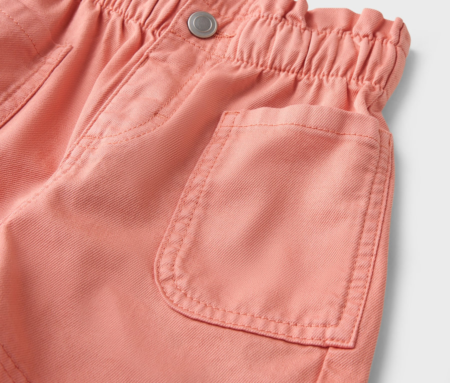 Gros plan sur un short couleur saumon avec une taille élastiquée et une poche plaquée.