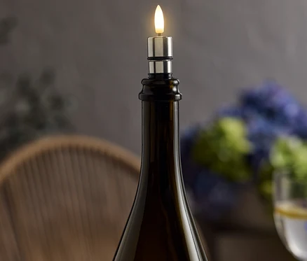 Sur une table, une bouteille de vin marron est coiffée d'une bougie LED argentée qui émet une lumière chaude.