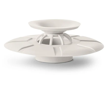 Un bouchon de drain couleur crème avec un design en forme d'assiette repose sur une surface blanche.