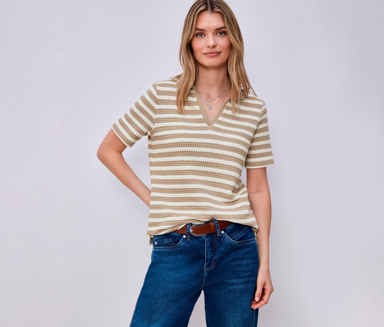 Une femme portant une ceinture marron et un jean porte un pull en maille rayé Street One. Elle pose devant un fond clair.