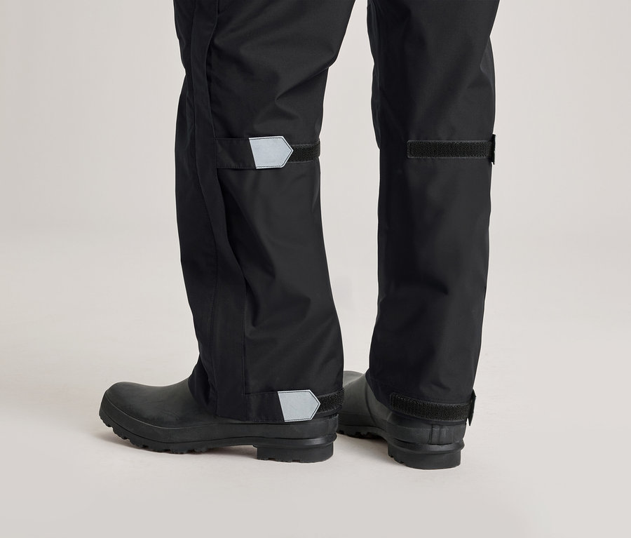 Gros plan sur le bas d'une personne portant un pantalon de pluie noir et des bottes en caoutchouc. Le pantalon a des détails réfléchissants.