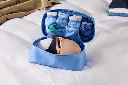 Organisateur de bagage bleu clair ouvert avec soutiens-gorge et sous-vêtements sur un drap blanc.