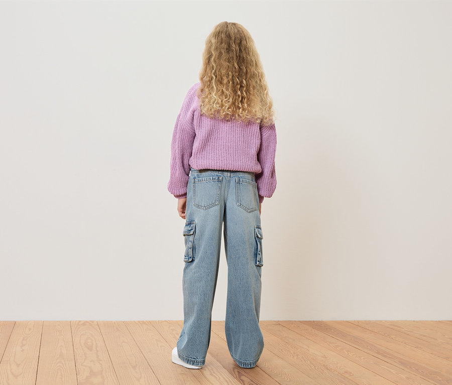 Vue arrière d'une fille aux boucles blondes portant un pull violet et un jean bleu clair avec des poches latérales.