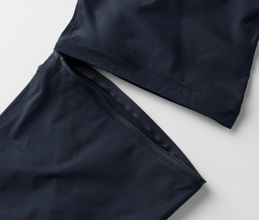Gros plan sur des jambes de pantalon bleu marine avec une fermeture éclair apparente sur un fond blanc.