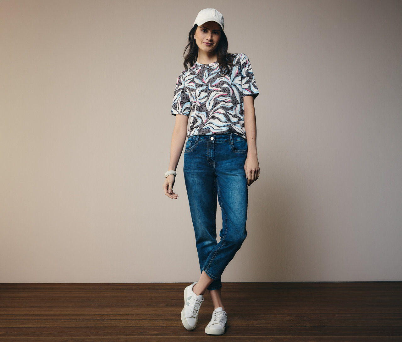 Femme portant un t-shirt manches courtes CECIL bleu et un jean CECIL « Scarlett », avec des chaussures et une casquette blanches.