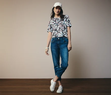 Femme portant un t-shirt manches courtes CECIL bleu et un jean CECIL « Scarlett », avec des chaussures et une casquette blanches.