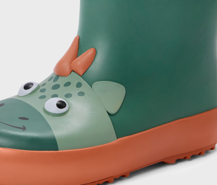 Gros plan sur une botte de pluie verte pour enfant avec une semelle orange et un motif de dinosaure.