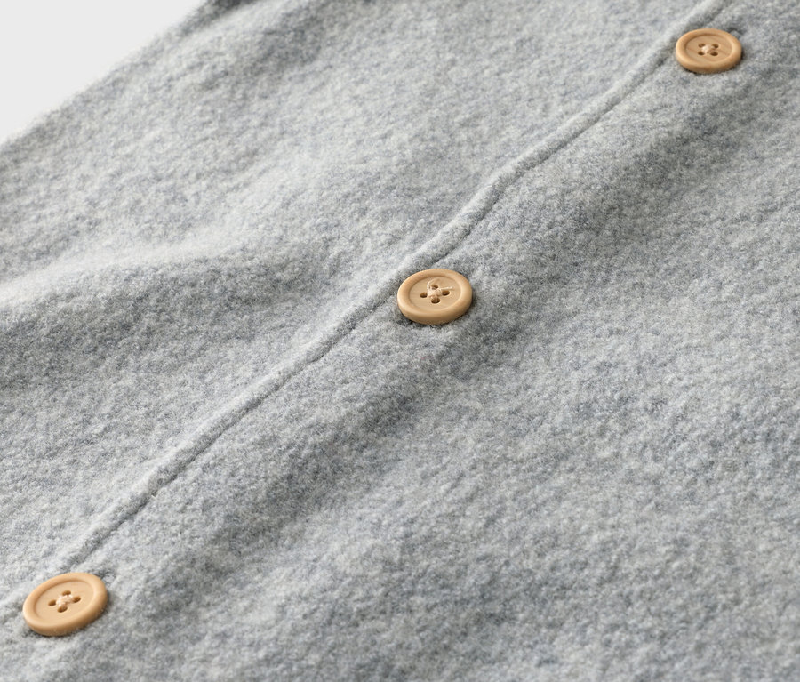 Gros plan sur un cardigan en tricot gris clair avec trois boutons marron clair.