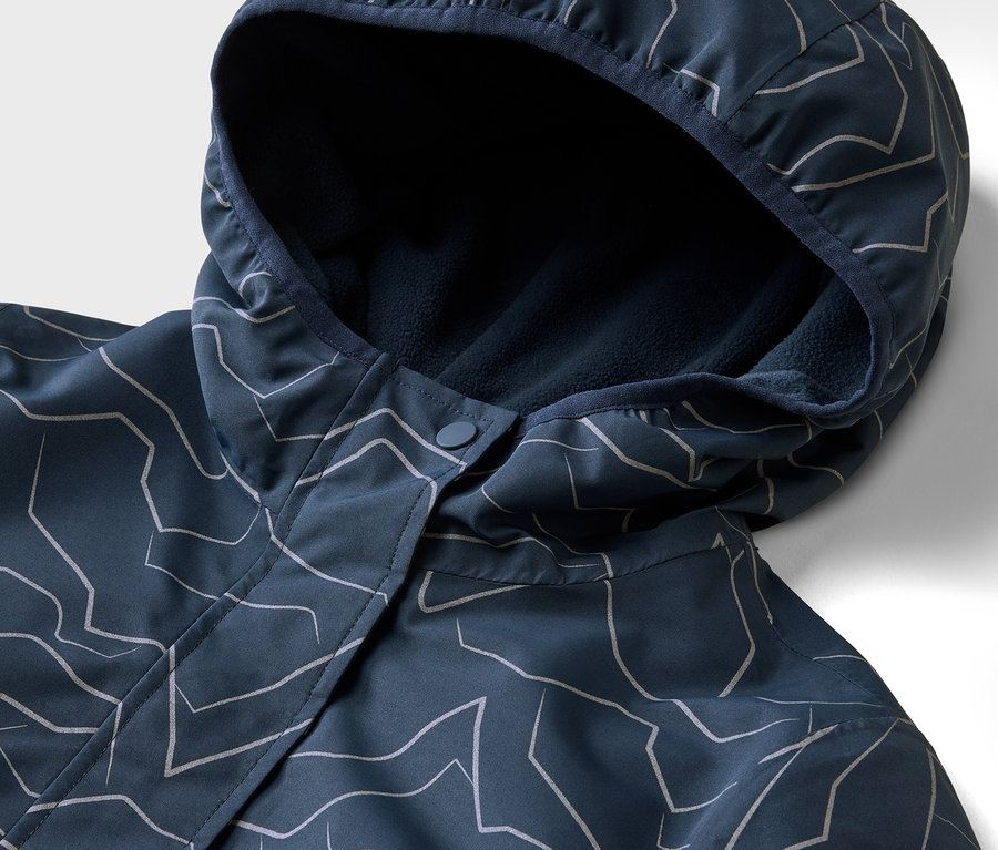 Gros plan d'une veste bleu marine à capuche avec un motif géométrique blanc. La capuche est doublée de polaire bleu marine.