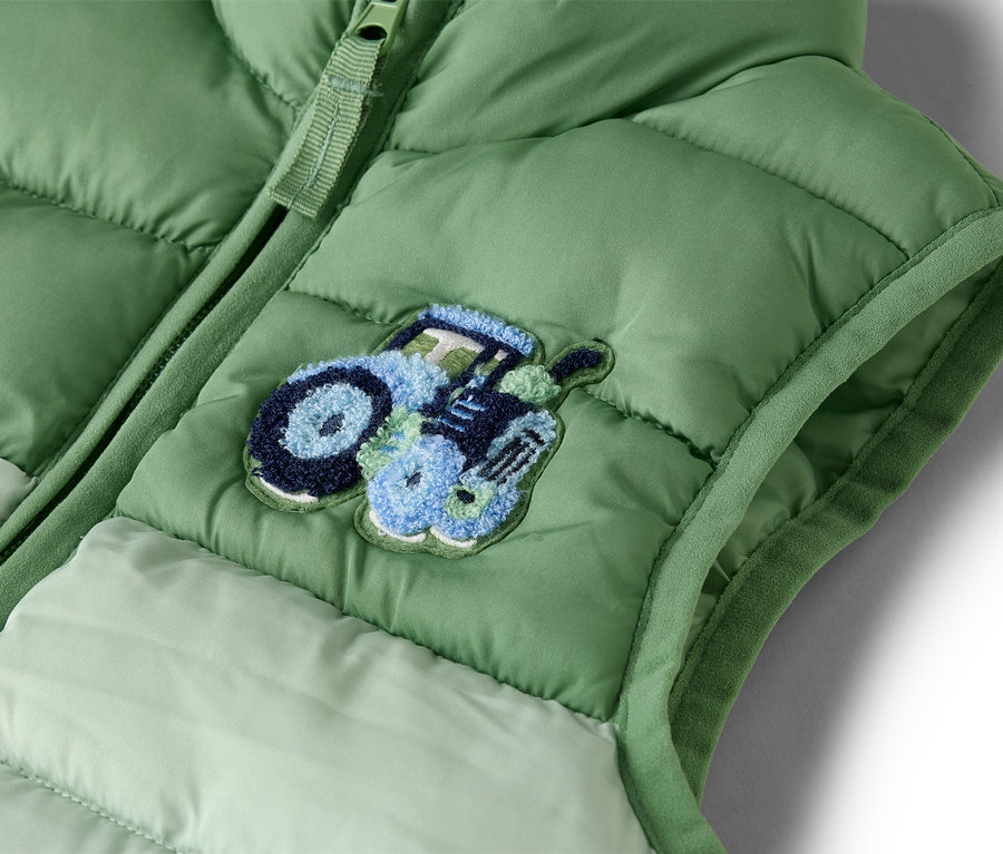 Gros plan sur un gilet matelassé vert clair avec une fermeture éclair et un appliqué de tracteur bleu.