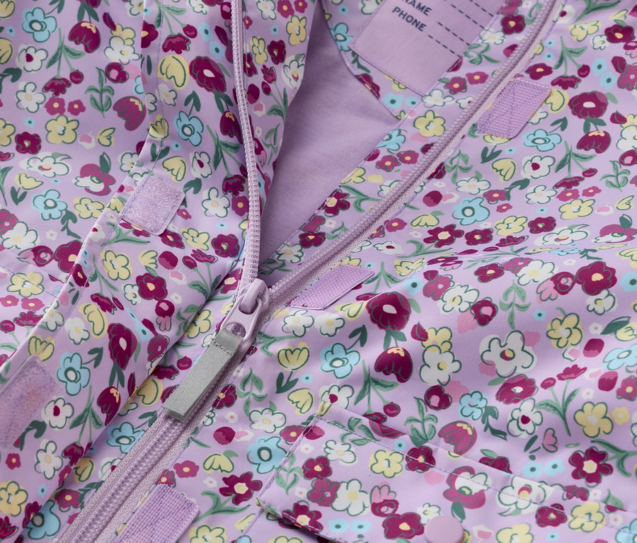 Gros plan d'une veste d'enfant violette à motif floral, ouverte par une fermeture éclair.